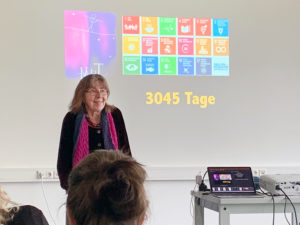 Margret Rasfeld spricht bei einer Fortbildung vor den Lernbegleiter:innen der Universitätsschule Dresden. Die Präsentation an der Wand hinter ihr zeigt "3045 Tage" und Symbole für verschiedene Fächer / Fachbereiche.