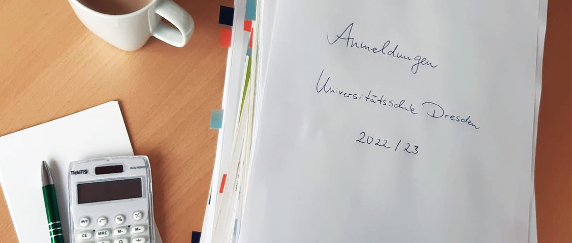 Großer Papierstapel mit Anemdlungen für das Schuljahr 2022/23, Kaffeetasse und Taschenrechner auf dem Schreibtisch.